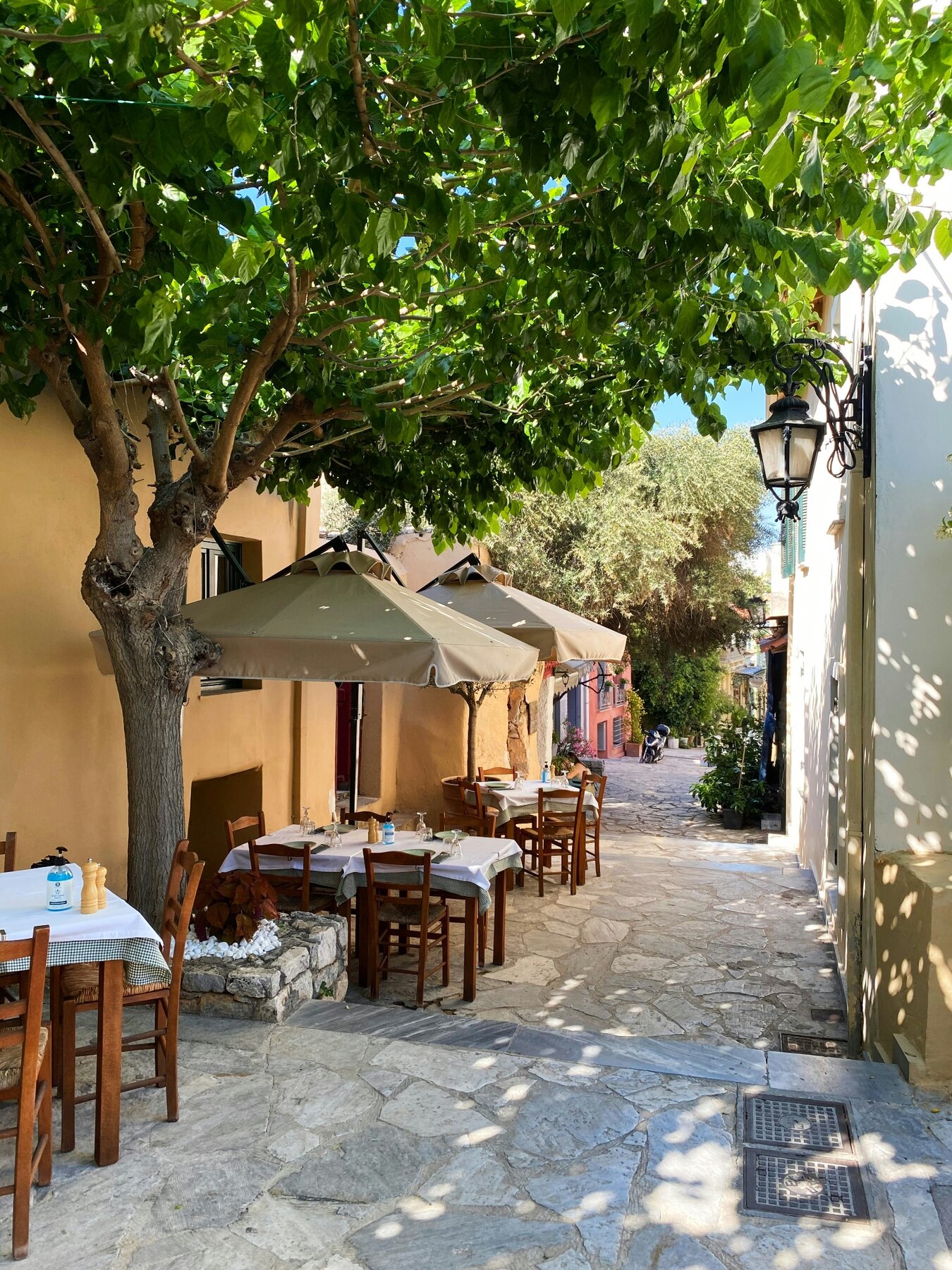 Shaded café tables on a narrow pedestrian lane in Athens