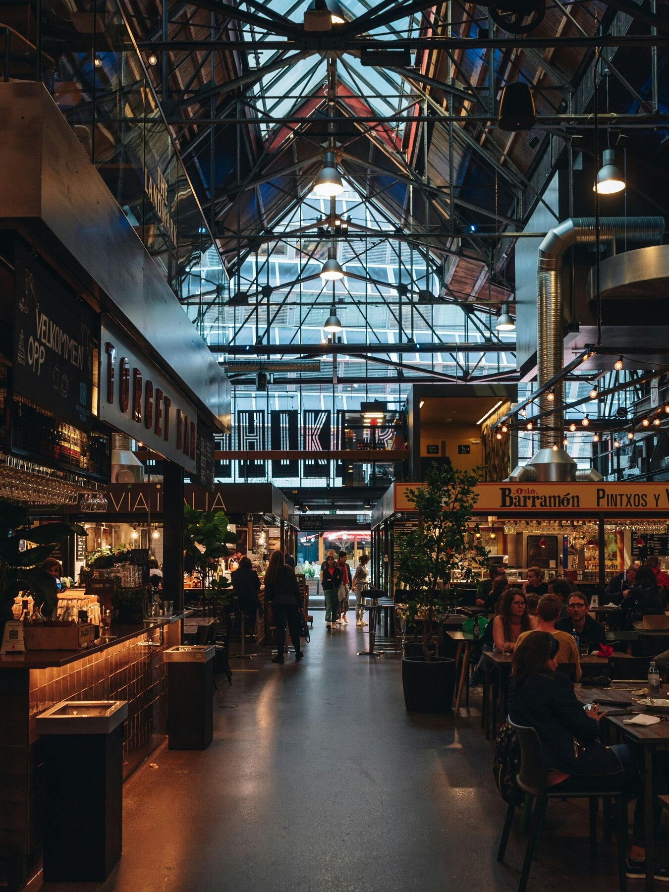 People beneath the glass roof of a busy Oslo food hall