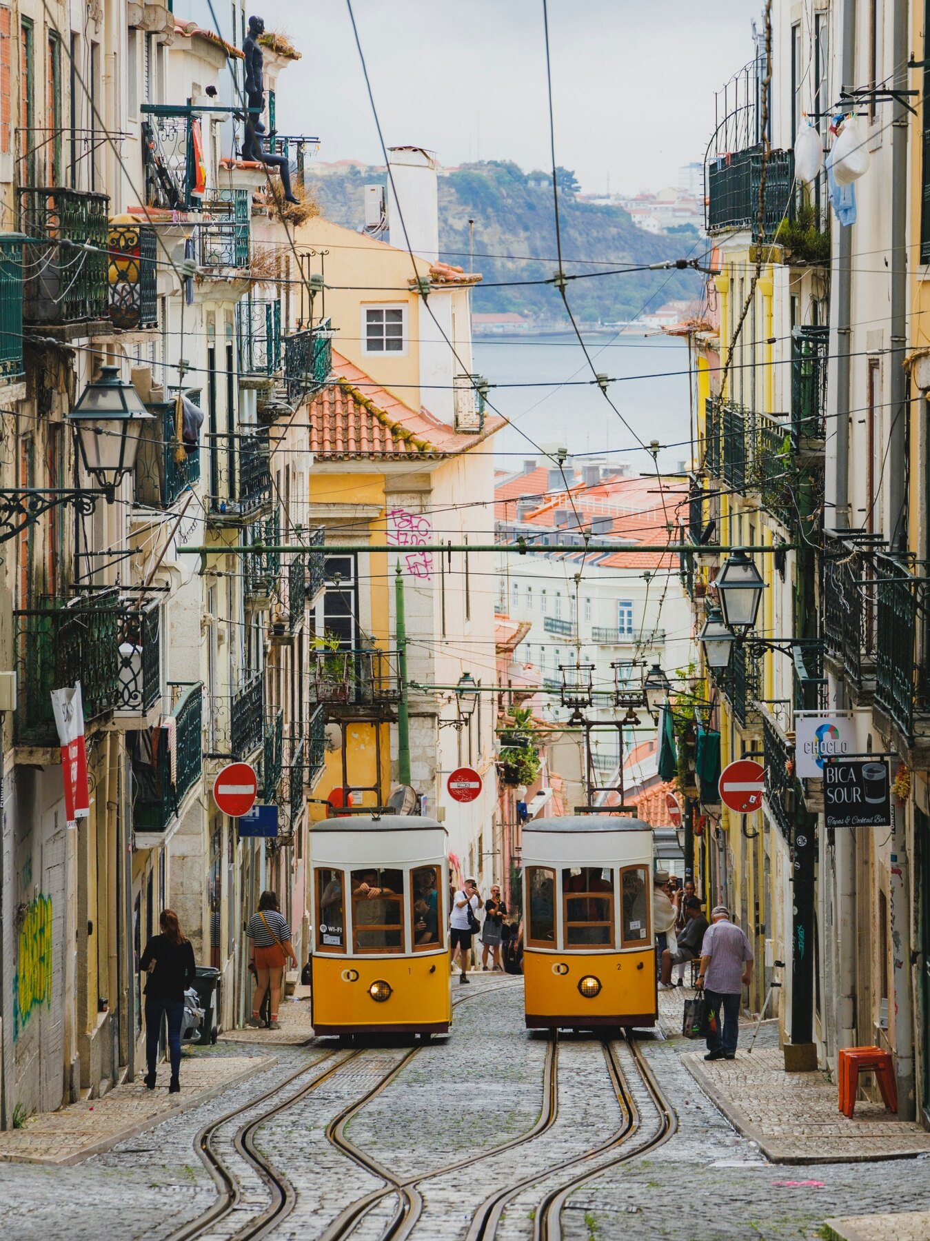 Two yellow trams passing on a steep Lisbon street