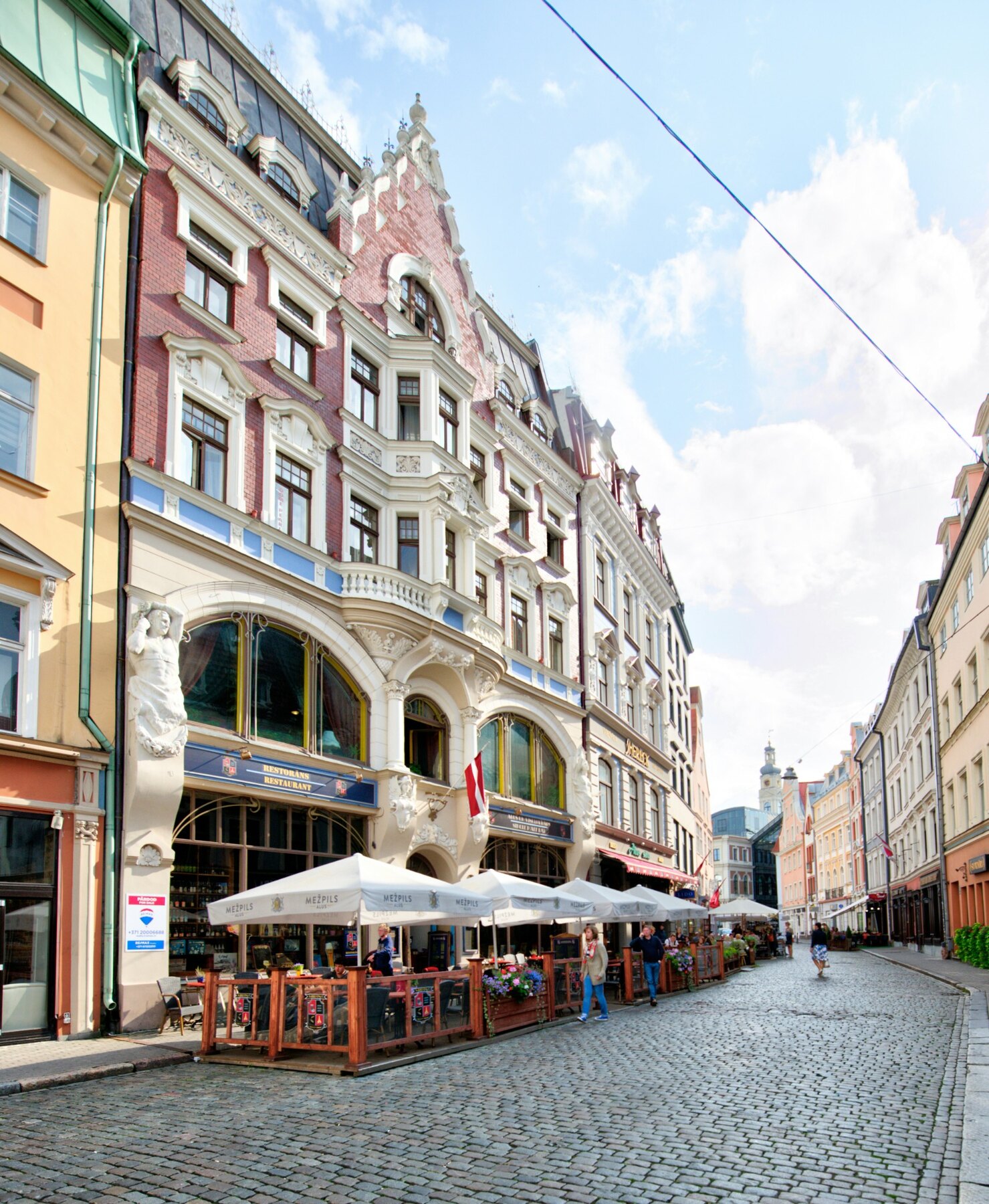 People at pavement cafés along a cobbled street in Riga