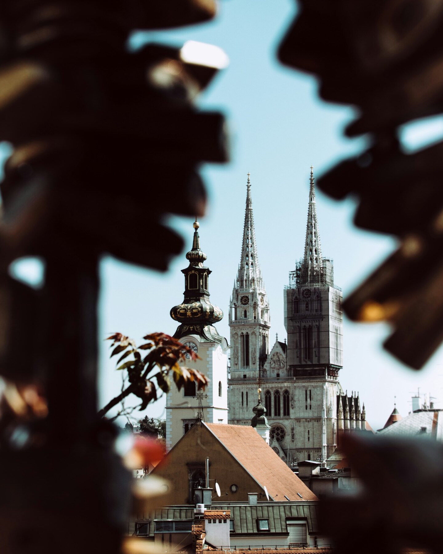 Zagreb Cathedral framed by dark leaves and nearby rooftops
