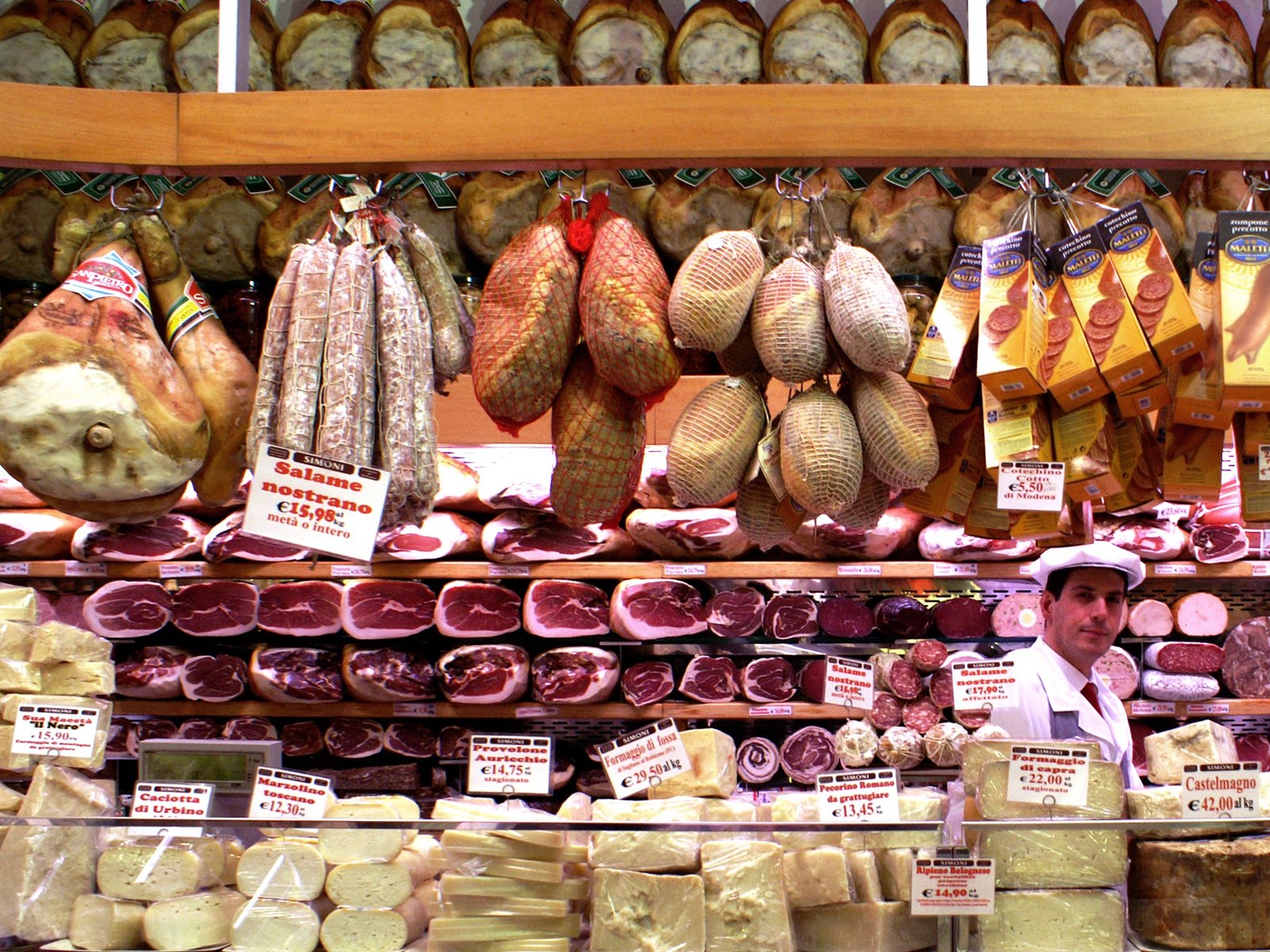 A Bologna food shop counter filled with hanging salumi, cured meats and Italian cheeses.