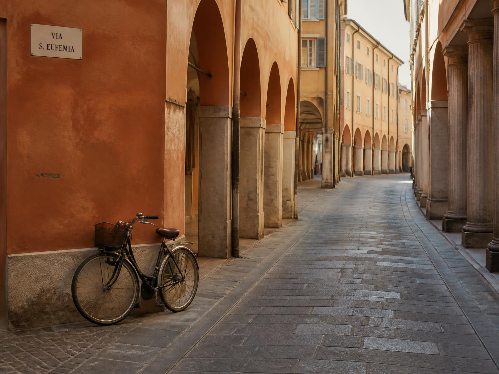 A quiet arcaded street in central Modena, with ochre walls and a bicycle leaning against a portico
